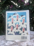 Book with painting of flowers and birds on back cover, sitting on coral block with flowering tree in background